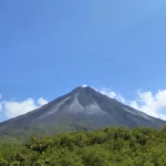 Scenic view of Arenal Volcano surrounded by lush rainforest in Costa Rica under a clear blue sky