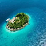 Aerial view of a small tropical island in the Solomon Islands surrounded by crystal-clear turquoise water and deep blue Pacific Ocean.