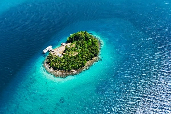 Aerial view of a small tropical island in the Solomon Islands surrounded by crystal-clear turquoise water and deep blue Pacific Ocean.