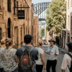 Walking tour group exploring the historic streets of The Rocks in Sydney with Sydney Harbour Bridge visible in the background