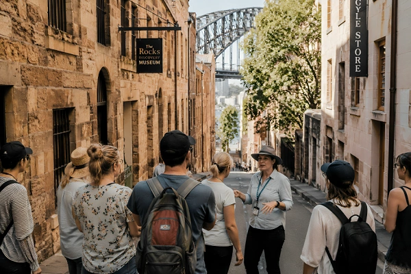 Walking tour group exploring the historic streets of The Rocks in Sydney with Sydney Harbour Bridge visible in the background